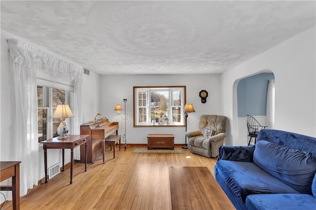 sitting room featuring light wood finished floors, visible vents, arched walkways, and a textured ceiling