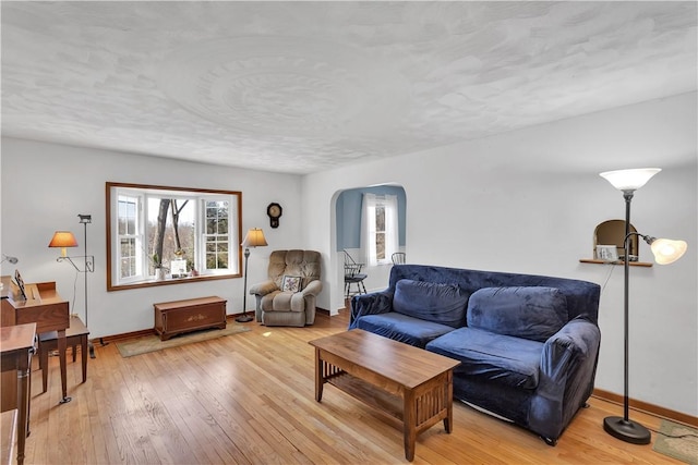 living room with arched walkways, light wood finished floors, and baseboards