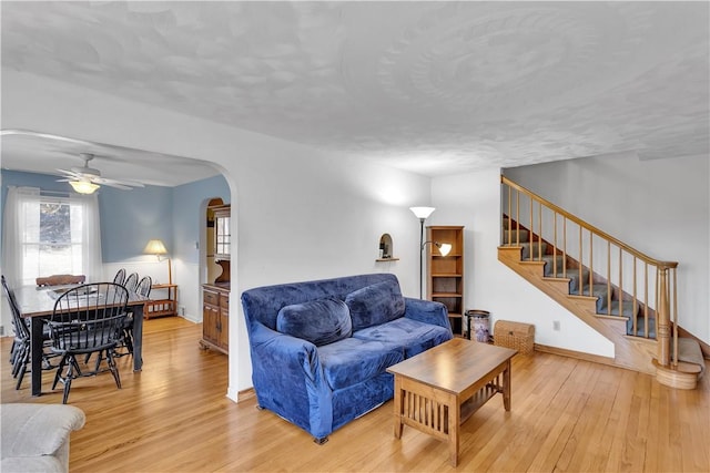 living area with light wood-type flooring, ceiling fan, stairs, and arched walkways