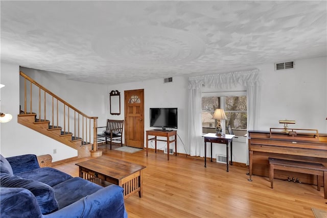 living room with stairs, visible vents, and wood finished floors