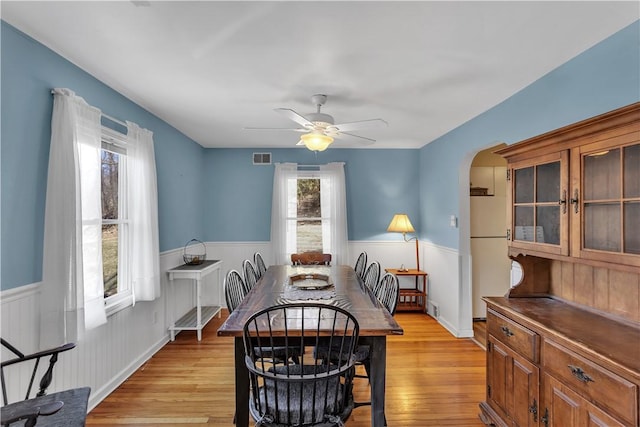 dining area featuring a wainscoted wall, arched walkways, and light wood-style floors