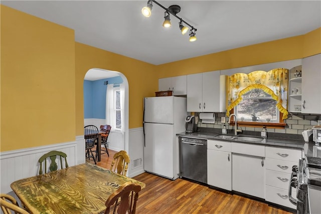 kitchen featuring arched walkways, dishwashing machine, a sink, freestanding refrigerator, and dark countertops