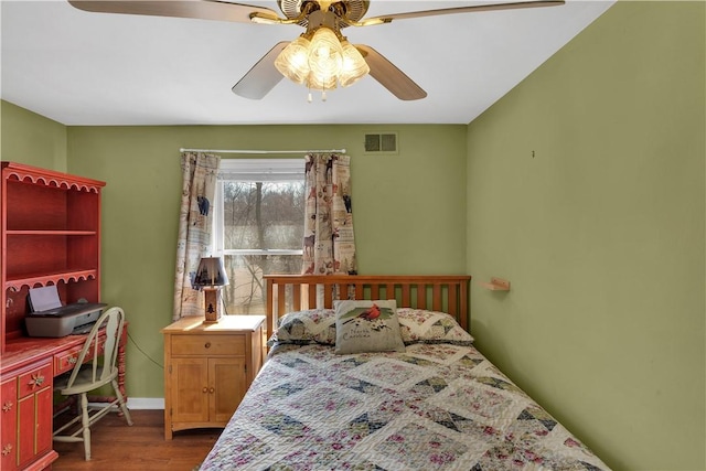 bedroom with a ceiling fan, visible vents, baseboards, and wood finished floors