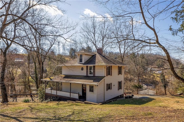 rear view of house featuring covered porch, roof with shingles, a lawn, and a chimney