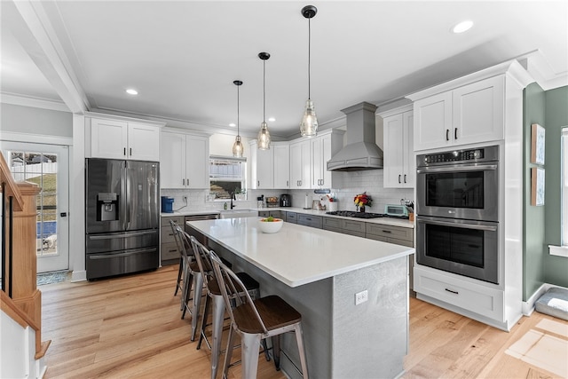 kitchen featuring a center island, a kitchen bar, appliances with stainless steel finishes, light wood-style floors, and wall chimney exhaust hood