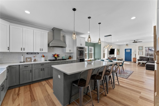 kitchen featuring premium range hood, gray cabinetry, open floor plan, gas stovetop, and double oven