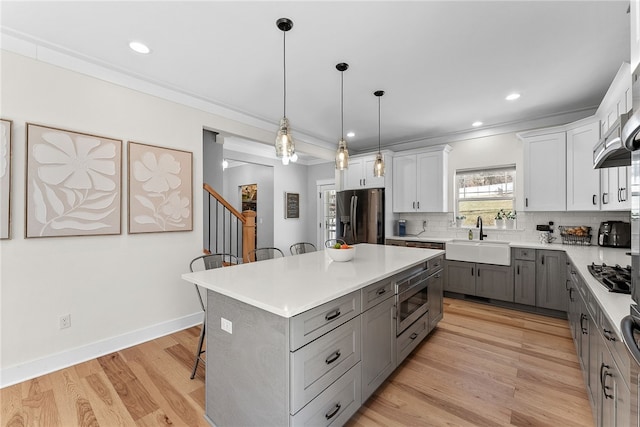 kitchen with gray cabinets, a sink, backsplash, stainless steel appliances, and light wood finished floors