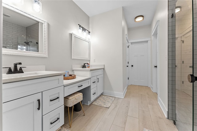 bathroom with wood finished floors, baseboards, tiled shower, two vanities, and a sink