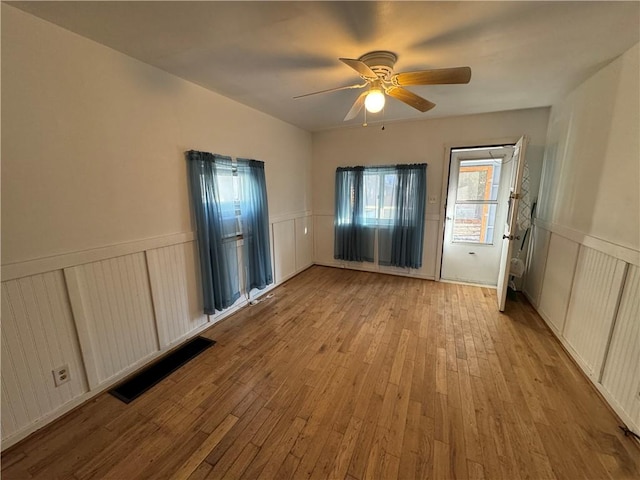 unfurnished bedroom featuring wood-type flooring, visible vents, a ceiling fan, and wainscoting