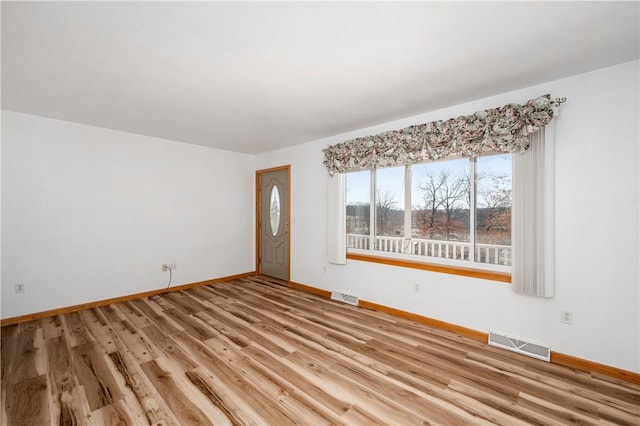 empty room featuring light wood-style flooring, visible vents, and baseboards