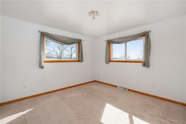 carpeted spare room featuring plenty of natural light, visible vents, and baseboards