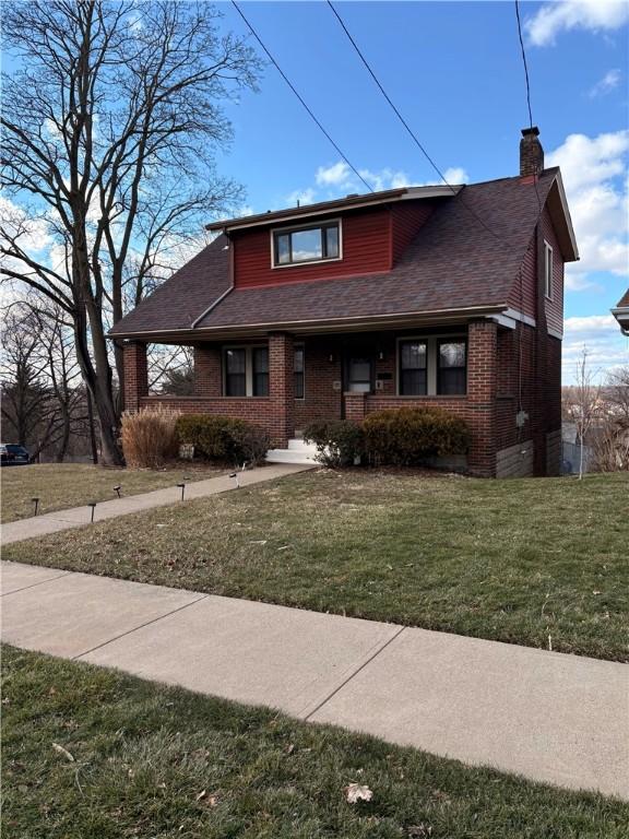 bungalow-style house featuring brick siding, a front lawn, roof with shingles, and a chimney