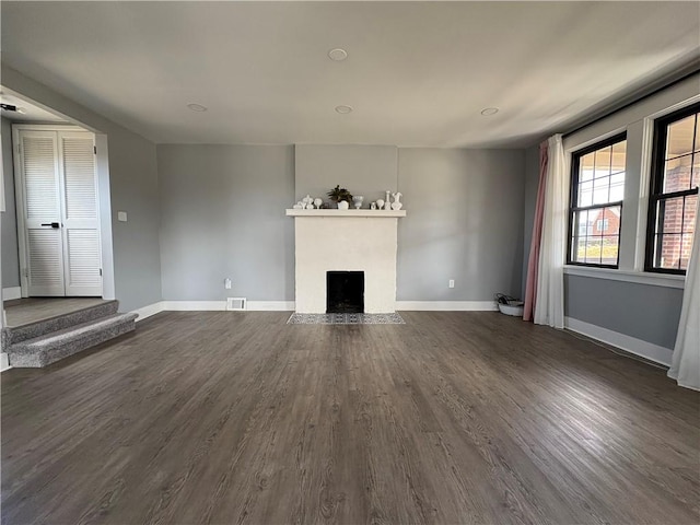 unfurnished living room featuring baseboards, a fireplace with flush hearth, visible vents, and dark wood-style flooring