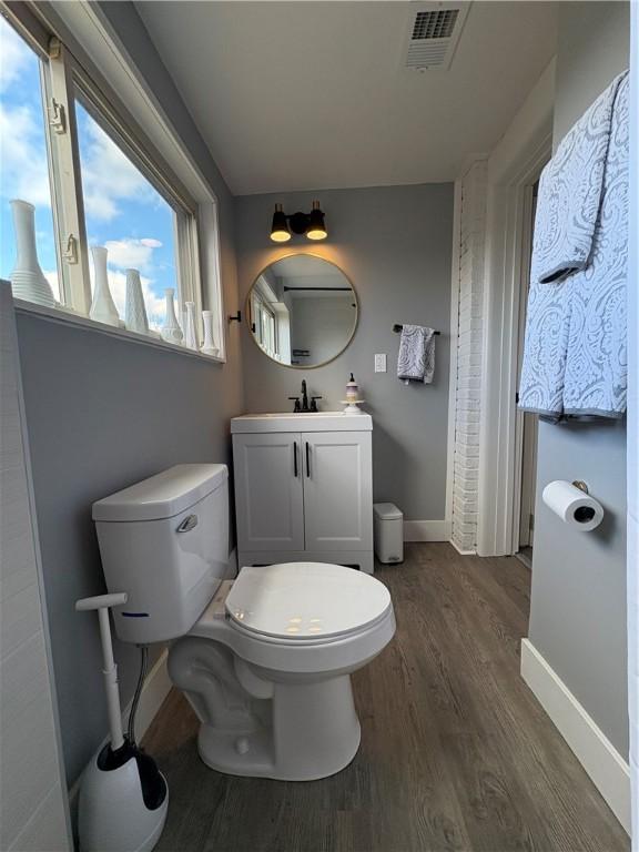 half bathroom with visible vents, baseboards, toilet, wood finished floors, and vanity