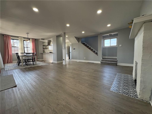 unfurnished living room featuring dark wood-style floors, plenty of natural light, stairs, and baseboards