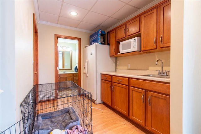 kitchen featuring light wood finished floors, light countertops, brown cabinetry, a sink, and white appliances