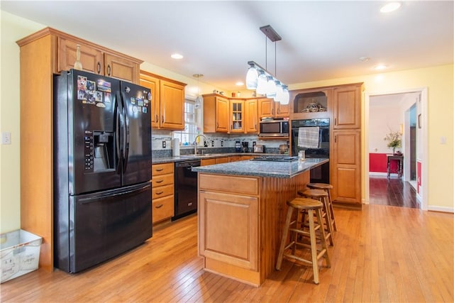 kitchen featuring light wood-style floors, a breakfast bar area, a center island, hanging light fixtures, and black appliances