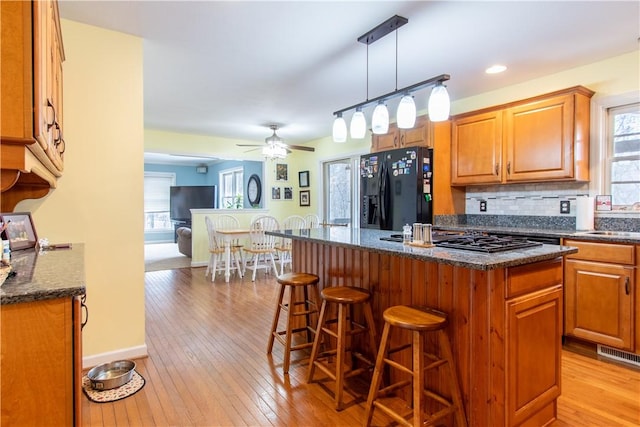 kitchen featuring light wood-type flooring, a kitchen breakfast bar, backsplash, and black appliances