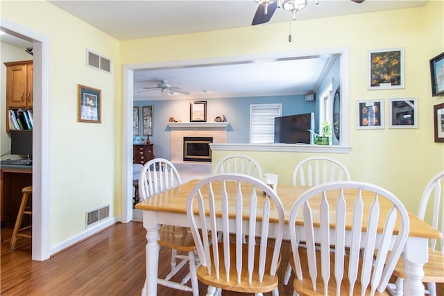 dining room with a ceiling fan, visible vents, a tiled fireplace, and wood finished floors