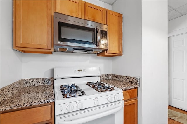 kitchen featuring brown cabinets, white range with gas cooktop, stainless steel microwave, and dark stone counters