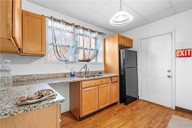 kitchen with light wood finished floors, a paneled ceiling, freestanding refrigerator, a sink, and light stone countertops