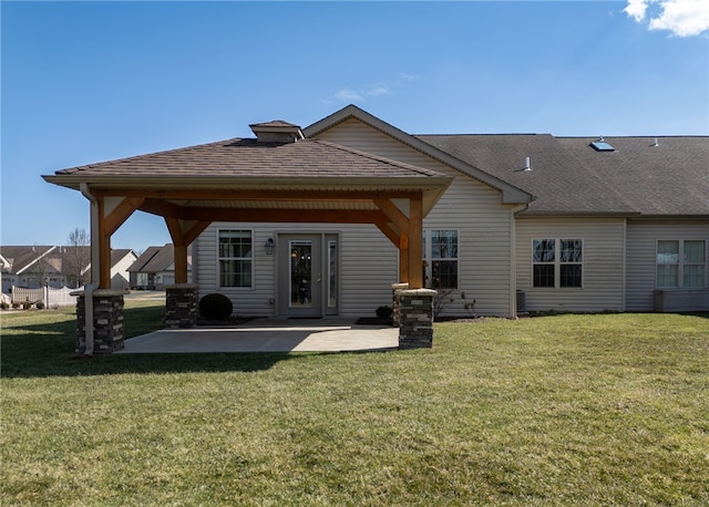 back of property featuring a shingled roof, a lawn, and a patio area