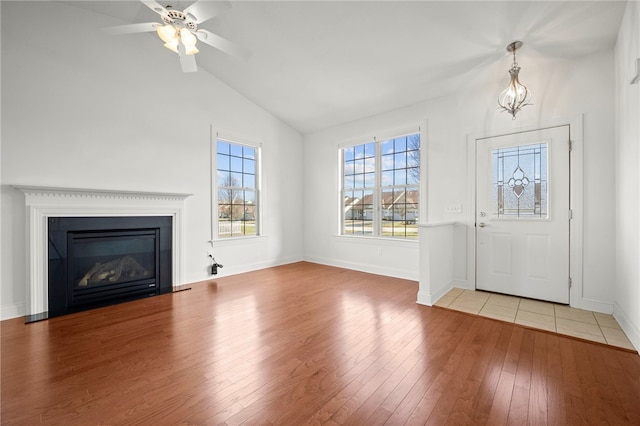 entryway featuring ceiling fan with notable chandelier, baseboards, vaulted ceiling, light wood finished floors, and a glass covered fireplace