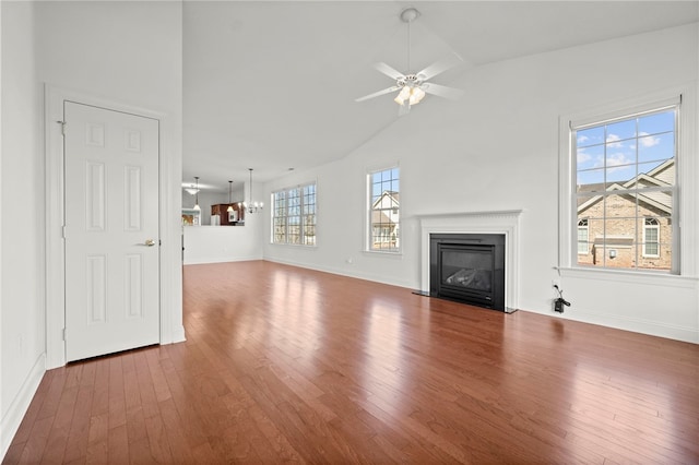 unfurnished living room with a fireplace with flush hearth, wood finished floors, high vaulted ceiling, baseboards, and ceiling fan with notable chandelier