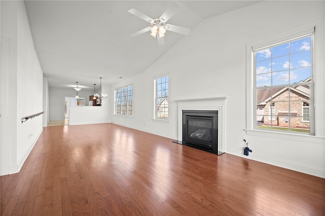 unfurnished living room with lofted ceiling, ceiling fan with notable chandelier, wood finished floors, baseboards, and a glass covered fireplace