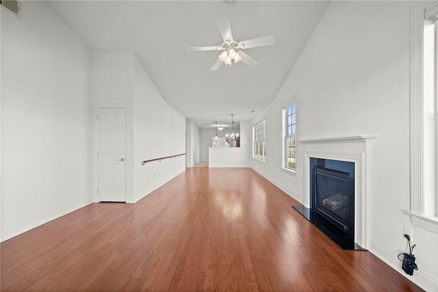 unfurnished living room featuring baseboards, visible vents, a glass covered fireplace, wood finished floors, and ceiling fan with notable chandelier