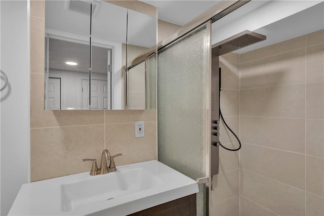 full bath with visible vents, backsplash, vanity, a shower stall, and tile walls