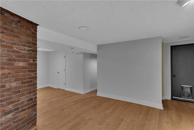 spare room with light wood-type flooring, baseboards, and a textured ceiling