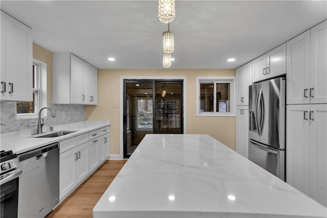 kitchen featuring stainless steel appliances, a sink, light wood-style floors, white cabinets, and tasteful backsplash