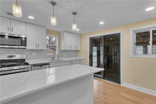 kitchen featuring a sink, appliances with stainless steel finishes, light wood-type flooring, decorative backsplash, and pendant lighting