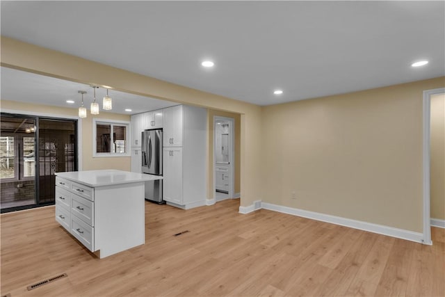 kitchen with white cabinets, stainless steel fridge, baseboards, and light wood finished floors