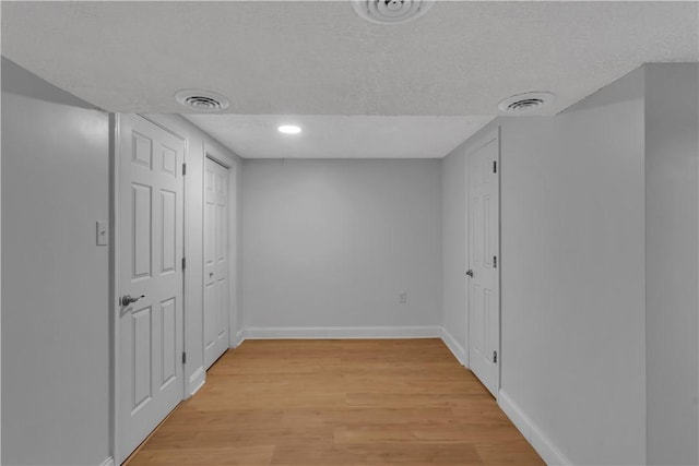 interior space with a textured ceiling, light wood-style flooring, visible vents, and baseboards