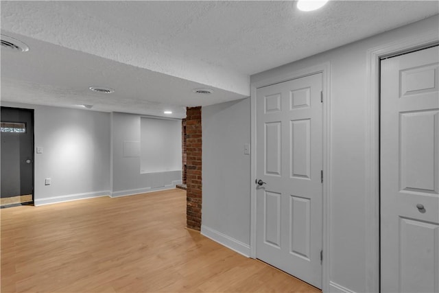 finished basement featuring light wood-style floors, baseboards, visible vents, and a textured ceiling