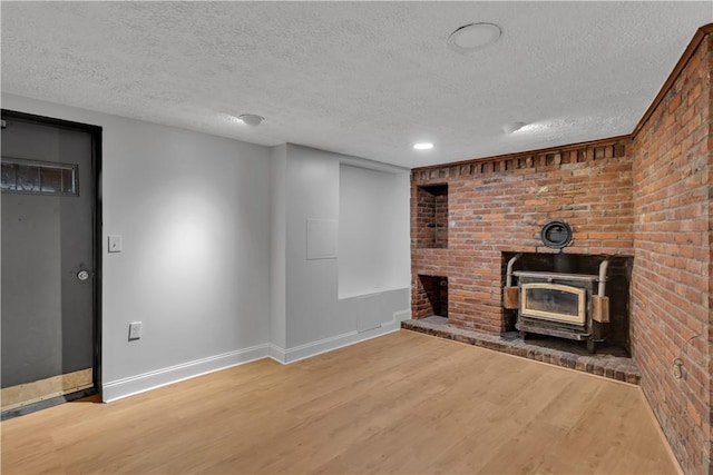 unfurnished living room with a textured ceiling, wood finished floors, a wood stove, and baseboards