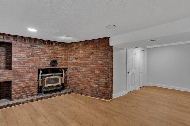 unfurnished living room with a wood stove, a textured ceiling, baseboards, and wood finished floors