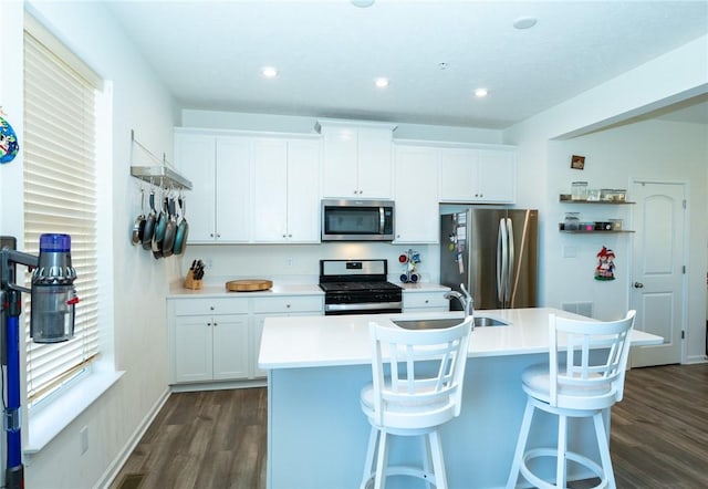 kitchen featuring white cabinets, dark wood finished floors, a kitchen island with sink, stainless steel appliances, and a sink