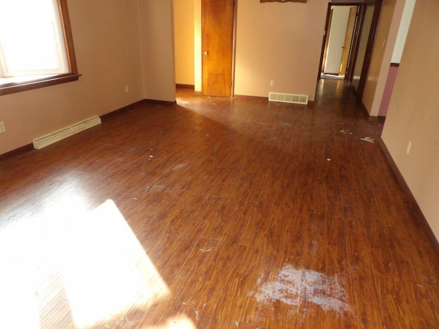 spare room with a baseboard heating unit, baseboards, visible vents, and wood finished floors