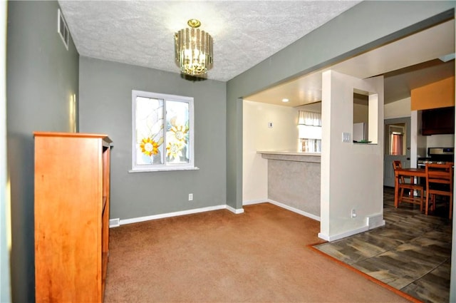 carpeted empty room featuring an inviting chandelier, visible vents, baseboards, and a textured ceiling