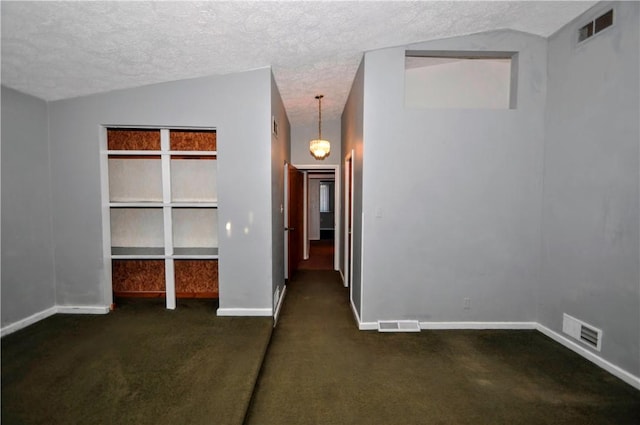 spare room featuring lofted ceiling, visible vents, dark carpet, and a textured ceiling