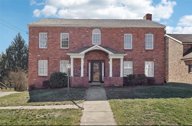 view of front facade with roof with shingles, a chimney, a front lawn, and brick siding