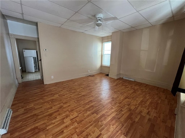 empty room with a drop ceiling, a baseboard radiator, wood finished floors, and visible vents