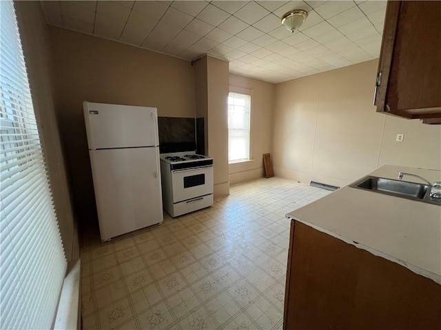 kitchen featuring a baseboard radiator, white appliances, a sink, light countertops, and light floors