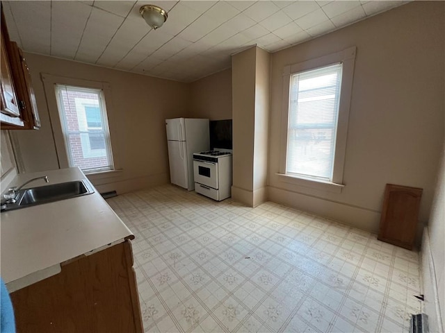 kitchen with light floors, light countertops, a sink, white appliances, and baseboards