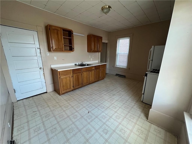 kitchen featuring white appliances, brown cabinetry, light countertops, light floors, and a sink