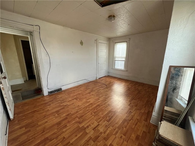 spare room featuring wood finished floors, visible vents, and baseboards