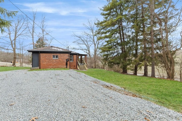 view of front of home with gravel driveway, a front lawn, and brick siding